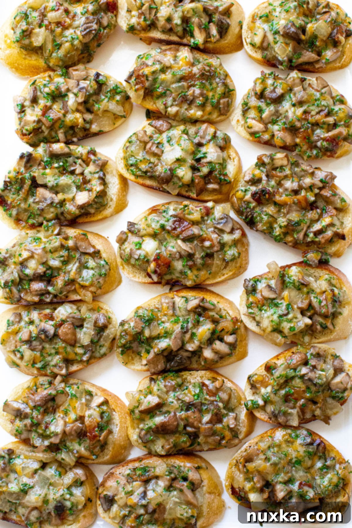 Close-up of hot mushroom canapés on a white platter, showcasing the golden melted cheese, sautéed mushrooms, caramelized onions, and bacon bits.