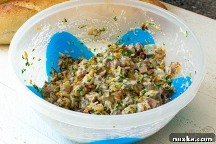 A food storage container filled with the mixed mushroom canapé topping: sautéed mushrooms, caramelized onions, bacon bits, cheese, and parsley.