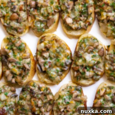 Close-up of baked hot mushroom canapés with melted cheese and fresh herbs on a white platter.