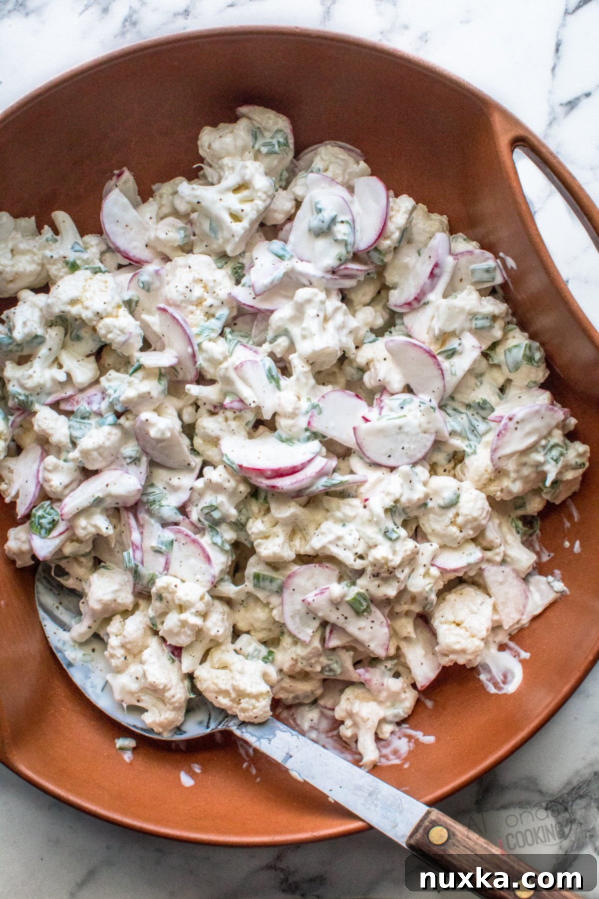 cauliflower salad with radish and green onions in a white bowl