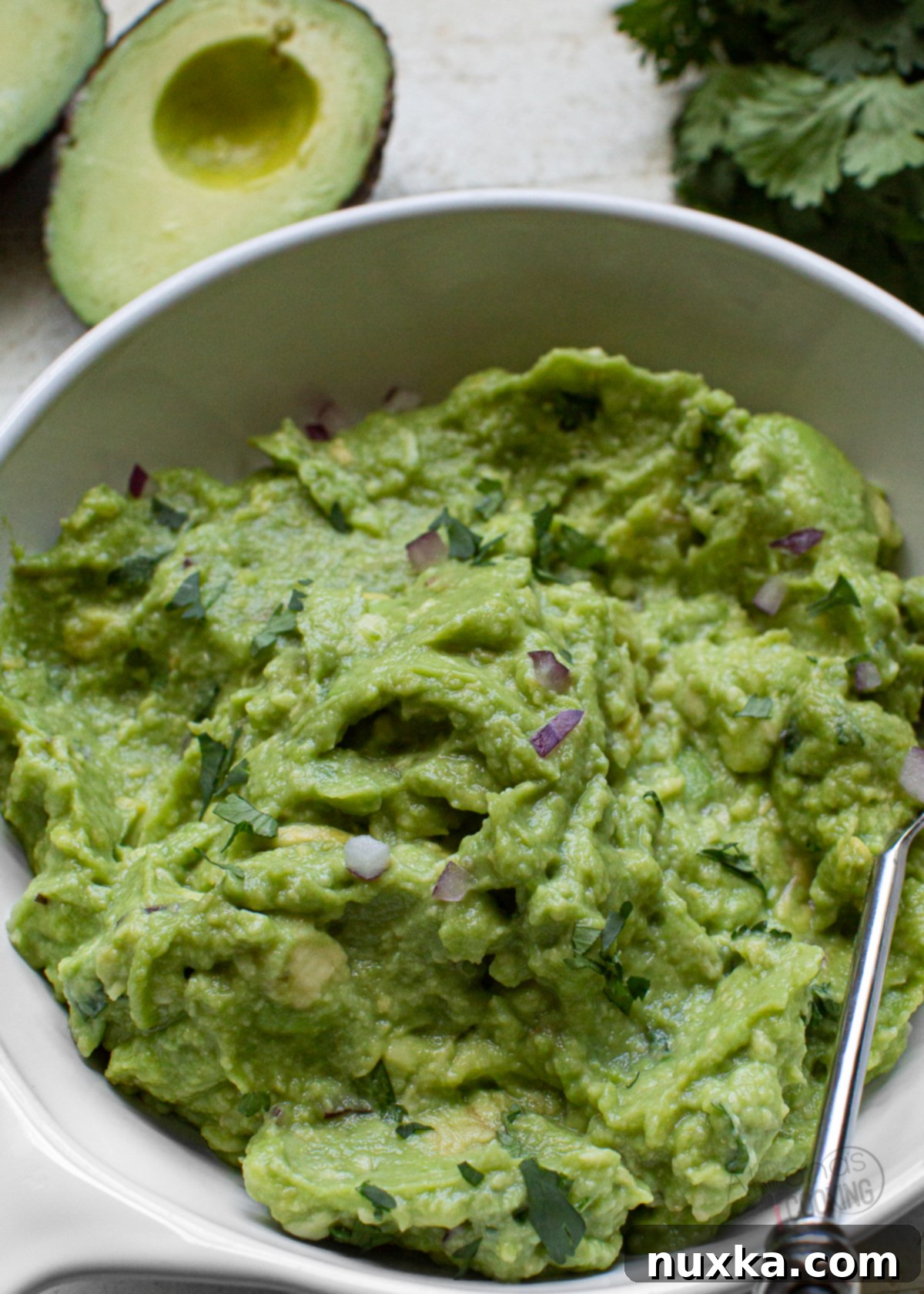 Close-up of freshly made Chipotle Guacamole, rich green with visible chunks of avocado, red onion, and cilantro, resembling the authentic restaurant style.