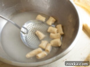 Dipping pretzel bites in baking soda solution with a slotted spoon