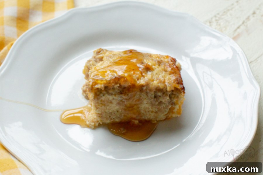 A slice of sausage breakfast casserole served on a plate, drizzled with sweet maple syrup, highlighting a delicious sweet and savory combination.