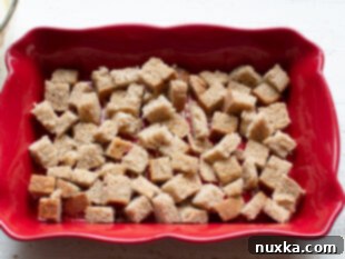 Cubed bread topped with cooked sausage and shredded cheese in a baking dish.