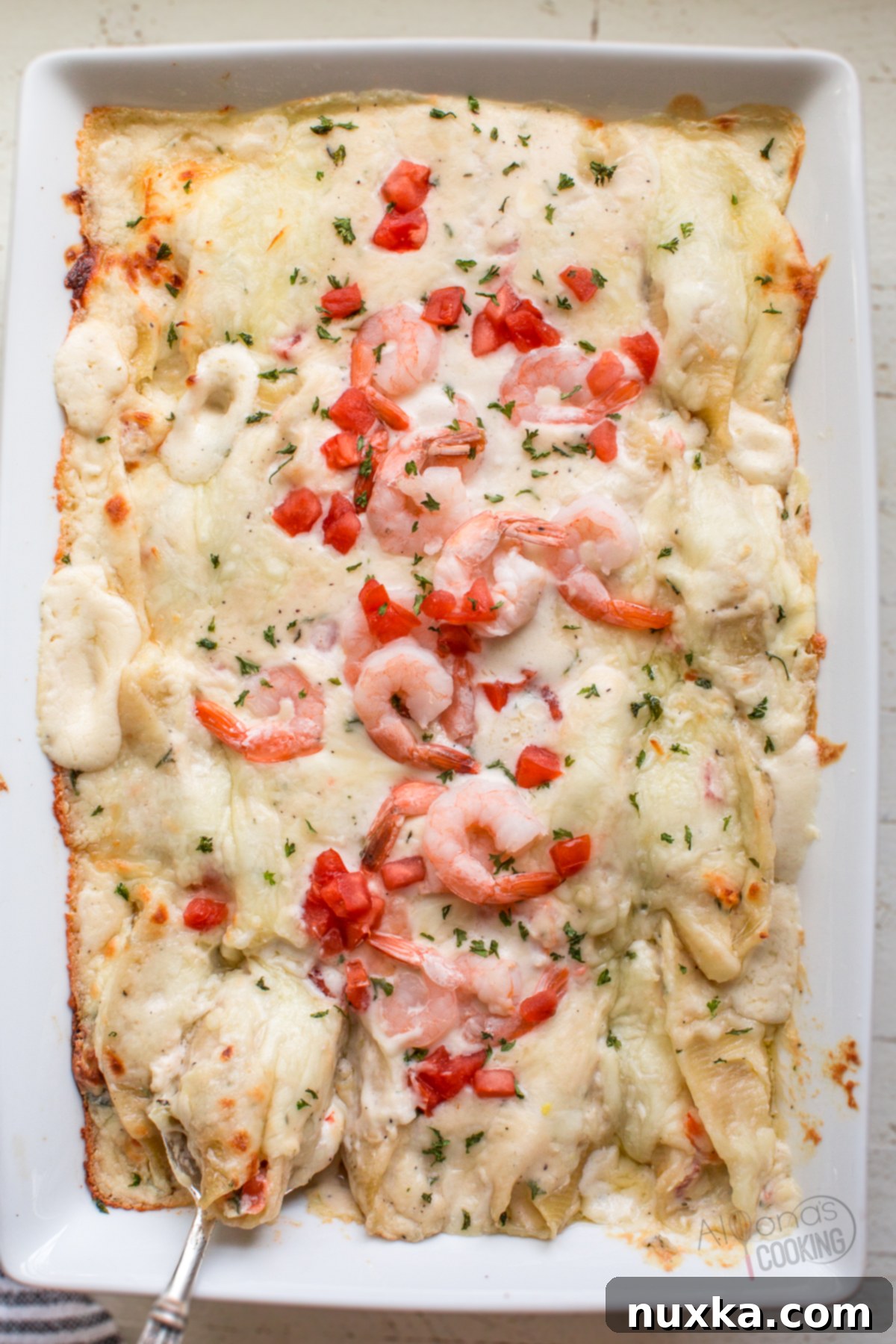 Jumbo stuffed shells covered in creamy Alfredo sauce, garnished with shrimp, tomatoes, and parsley.