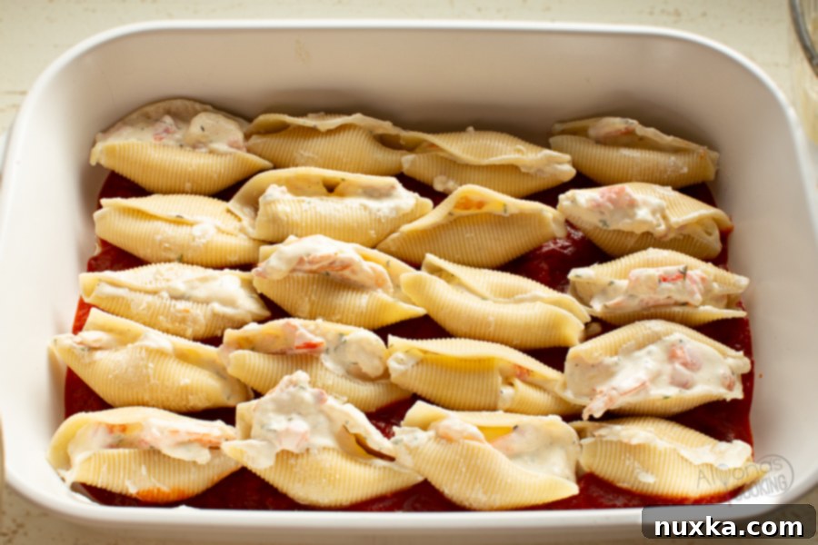 Shrimp stuffed shells arranged neatly in rows in a baking dish, covered with marinara sauce and ready for the oven.