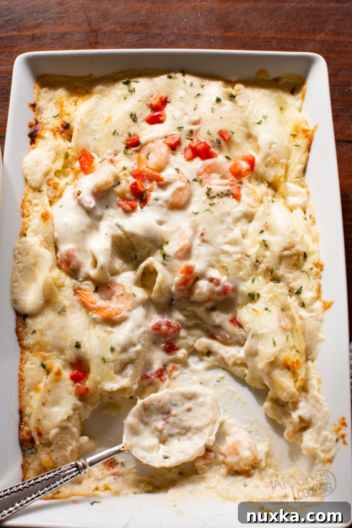 A close-up of baked jumbo shells in creamy Alfredo sauce, garnished with fresh herbs and tomatoes.