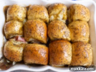 Baked ham and cheese sliders with melted cheese and golden poppy seeds.
