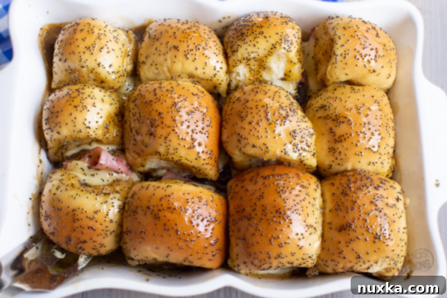 Close-up shot of baked ham and cheese sliders with a glossy poppy seed glaze, ready to serve.