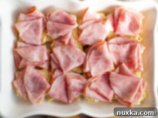 Layered sweet bread with ham slices for sliders in a baking dish.