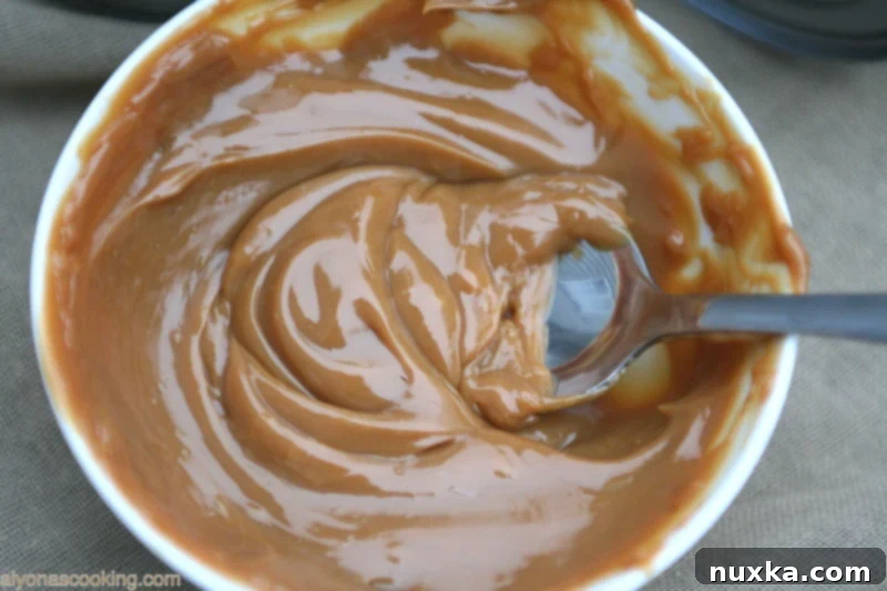 A close-up view of a spoon dipping into rich, creamy homemade Dulce de Leche caramel sauce.