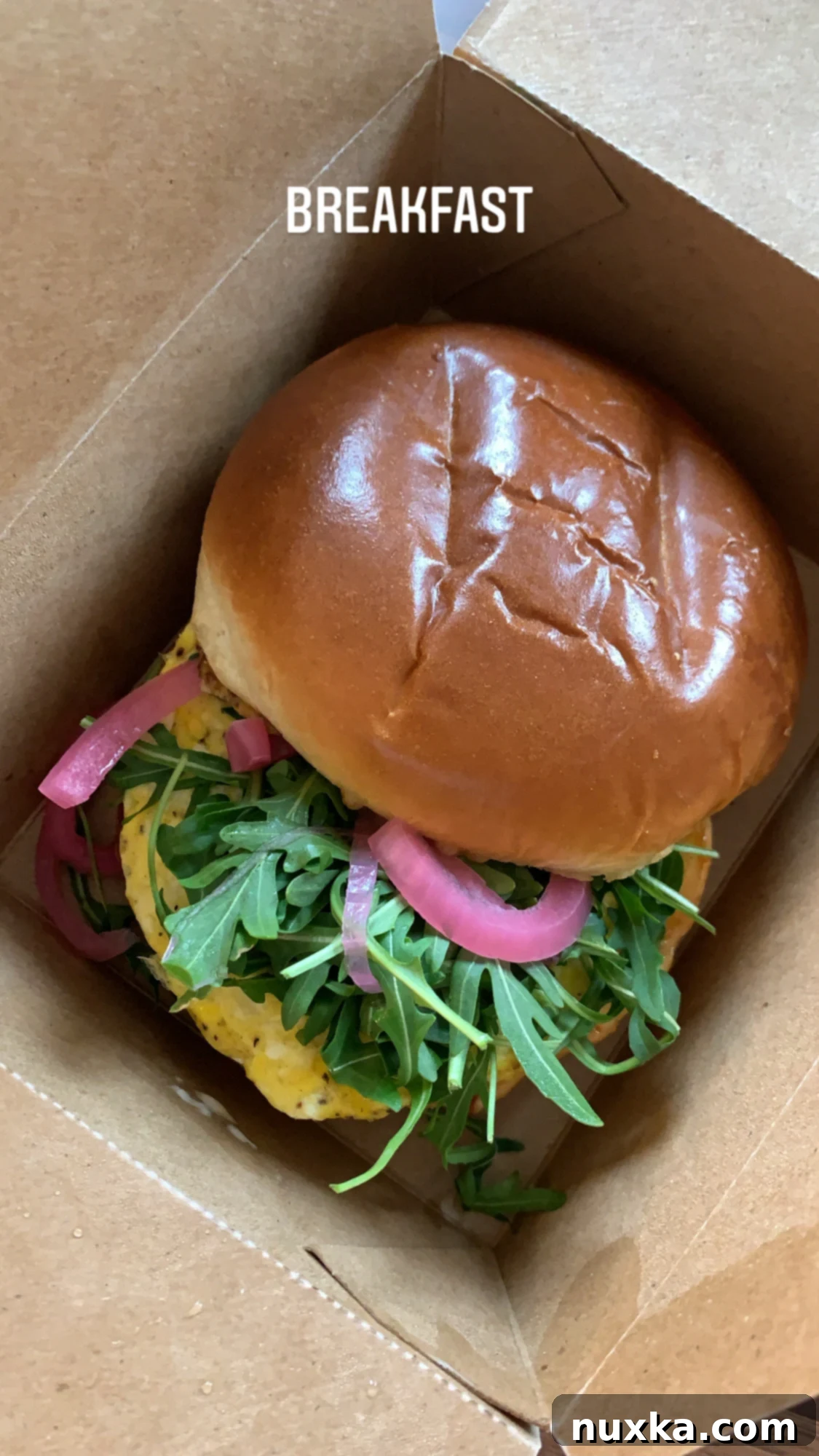 Original egg sandwich from Steadfast Coffee cafe, showcasing fluffy scrambled eggs, grainy mustard, Calabrian mayo, pickled red onions, and fresh arugula on a toasted brioche bun