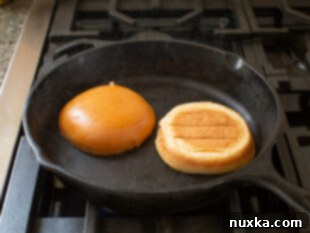 Brioche buns being toasted until golden brown in a cast iron pan for the egg sandwich recipe