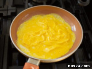 Scrambled eggs being cooked omelet-style in a small pan, pushed gently towards the center