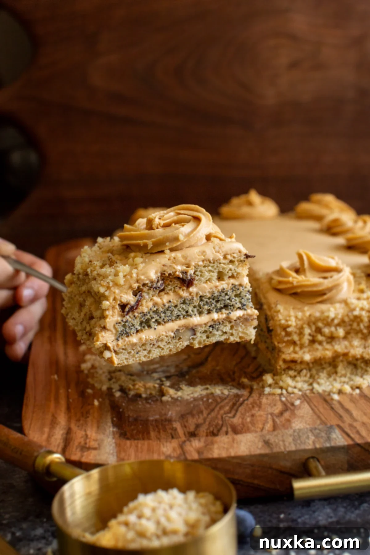 A perfectly sliced piece of Ukrainian poppy seed cake, showing its distinct layers of poppy seeds, walnuts, and raisins, topped with creamy frosting
