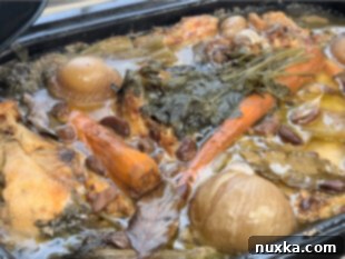 Large batch of chicken broth simmering in a roaster oven with vegetables and herbs added.