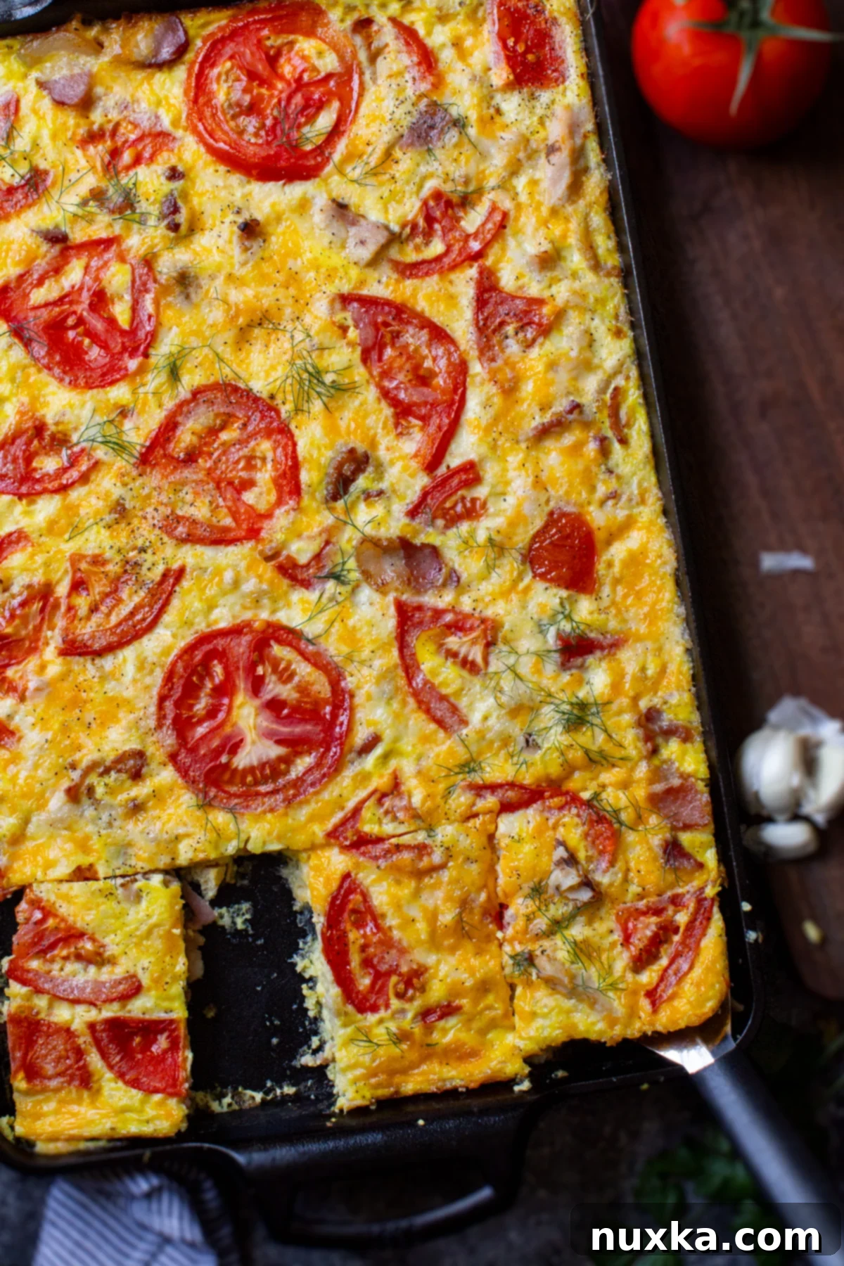 A cheesy egg frittata casserole baked in a cast iron pan with bacon, garlic, and fresh tomatoes