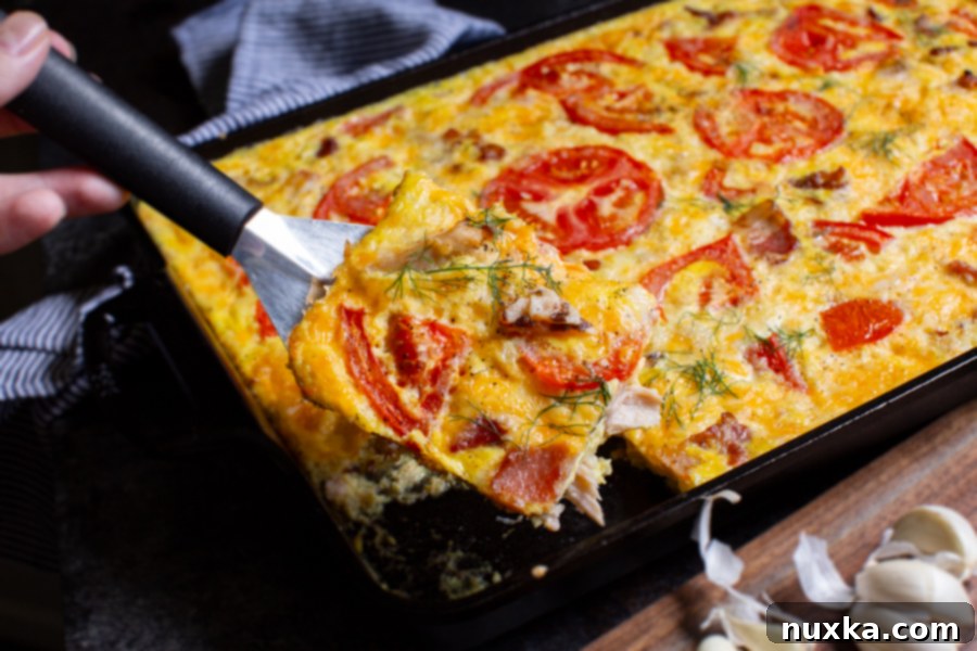 A close-up view of a baked frittata casserole with golden-brown edges, topped with melted cheese and fresh tomato slices.