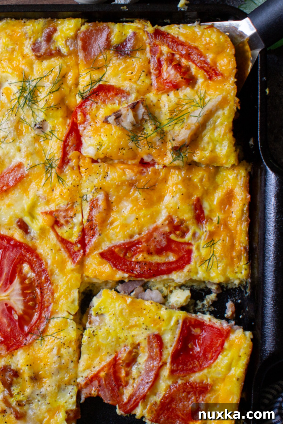 A close-up of a generously topped frittata casserole with melted cheese, crispy bacon, and fresh tomatoes, ready to be sliced.