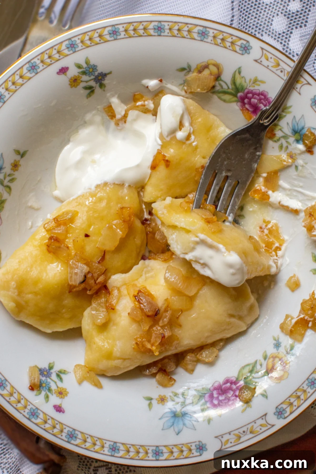 Close-up of potato pierogi topped with sour cream and caramelized onions