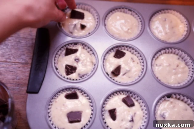 Muffin cups filled with banana chocolate chip batter, garnished with extra chocolate chunks