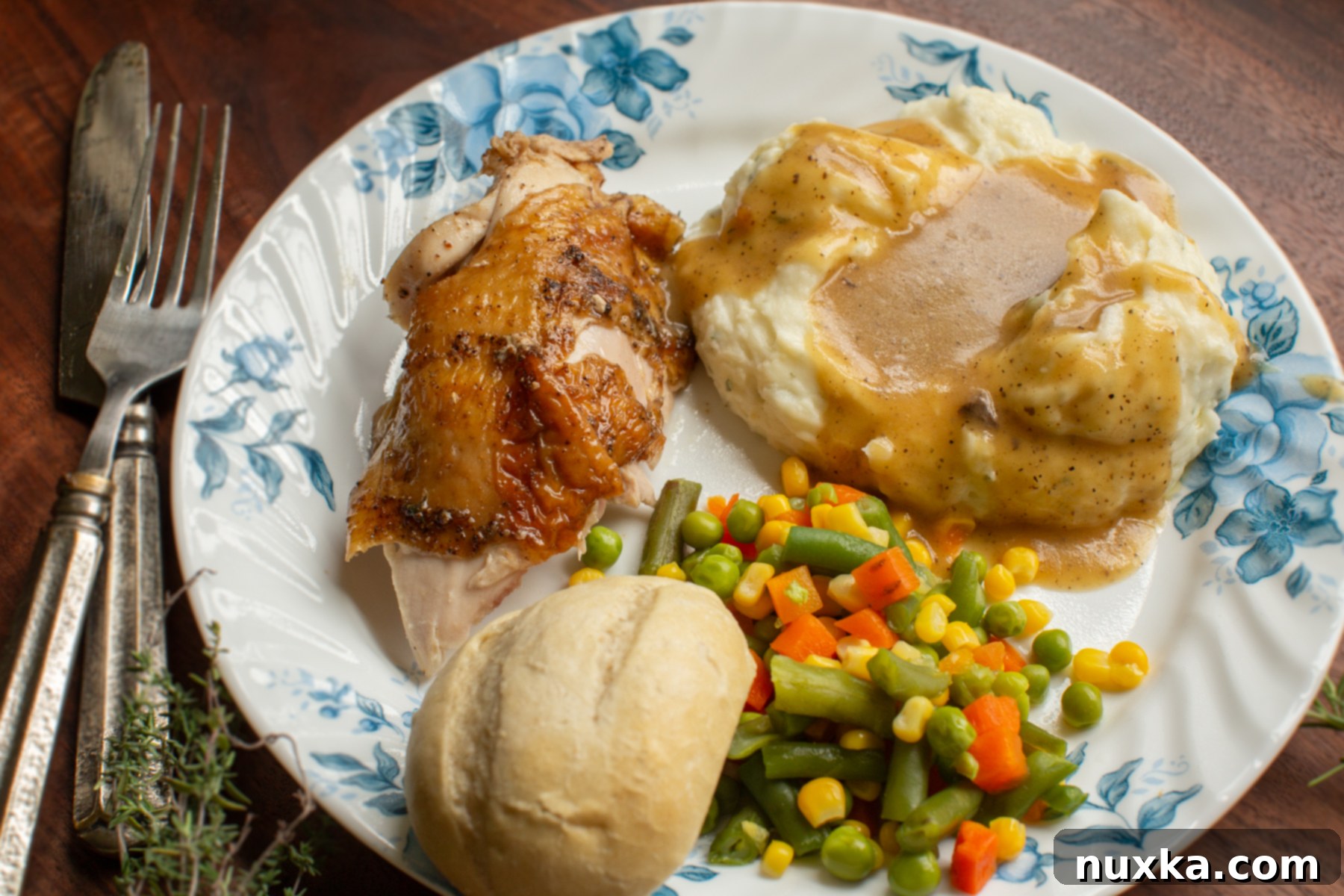 sliced roasted chicken plated with a dinner roll, mashed potatoes with gravy, and steamed vegtables 