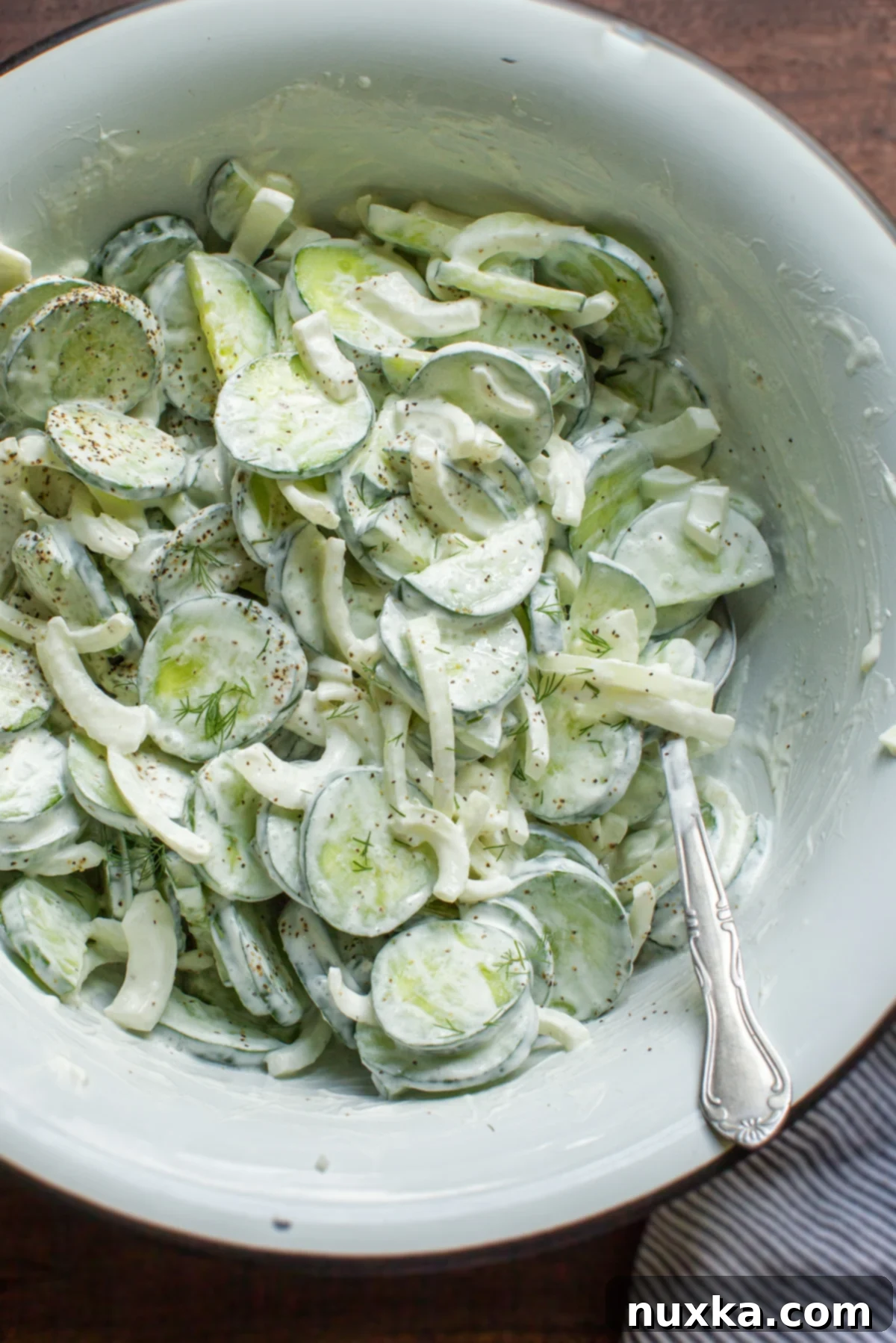 creamy cucumber onion salad in a white enamel bowl