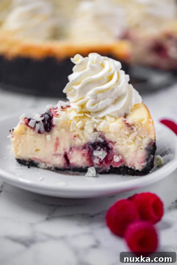Cheesecake Factory-style White Chocolate Raspberry Swirl Cheesecake topped with elegant white chocolate shavings and a dollop of whipped cream