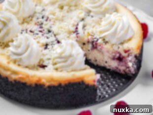 Cheesecake Factory-style white chocolate raspberry truffle cheesecake topped with white chocolate shavings and whipped cream topping, featuring a chocolate Oreo crust