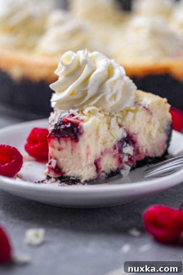 A perfectly sliced White Chocolate Raspberry Swirl Cheesecake, a homemade Cheesecake Factory White Chocolate Raspberry Truffle copycat, topped with delicate white chocolate shavings and creamy whipped cream