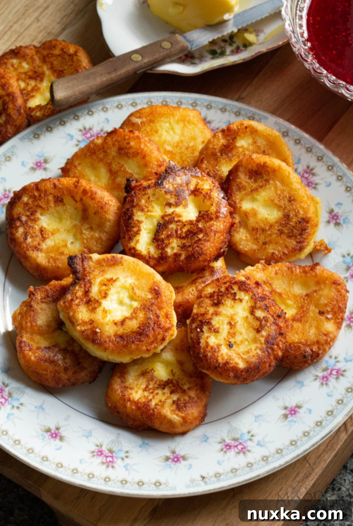 Russian Syrniki recipe with farmers cheese (cottage cheese), eggs, flour, sugar, and salt. Plated on a vintage plate with butter and raspberry sauce (jam.)