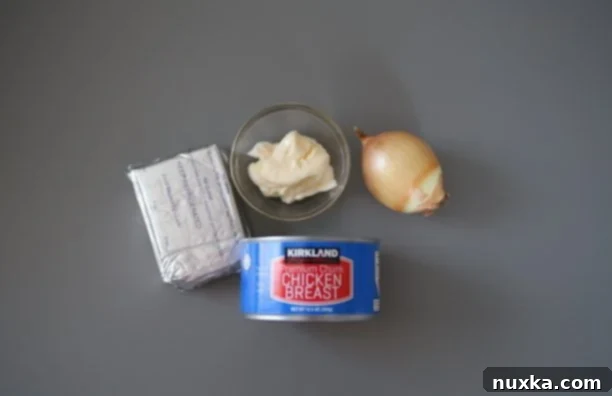 Bowl of chicken salad spread ingredients: canned chicken, cream cheese, mayonnaise, and diced sweet onion.
