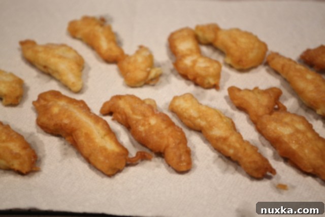 Freshly fried golden chicken fingers draining on paper towels.