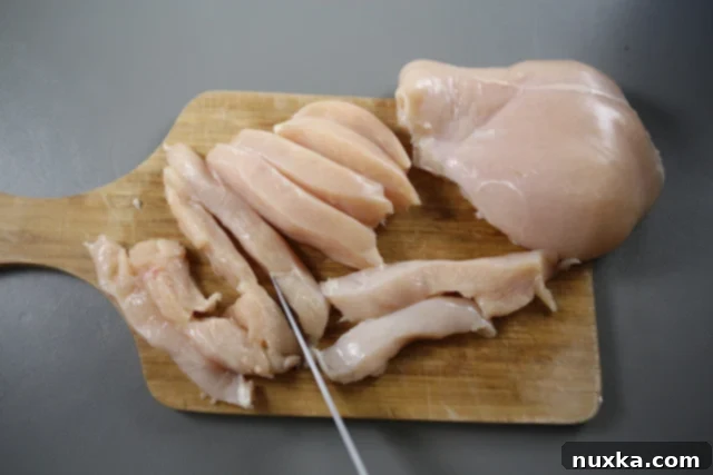 Chicken breasts being cut into strips on a cutting board.