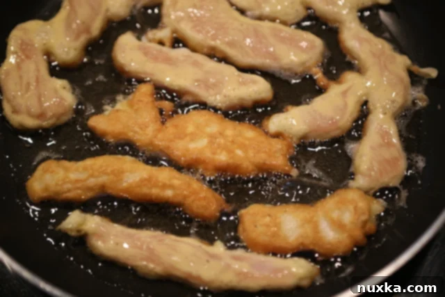 Golden brown chicken fingers frying in hot oil in a skillet.