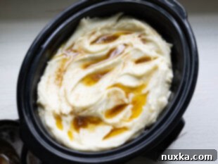 Fluffy mashed potatoes being transferred into a greased crockpot for keeping warm.