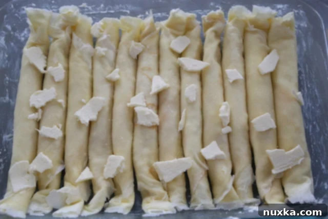 layers of cottage cheese crepes with butter pats on top, ready for baking