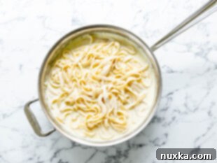 Adding the cooked fettuccine pasta to the homemade Olive Garden Alfredo Sauce