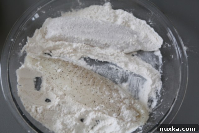 Tilapia fillets being dredged in flour for a crispy coating.