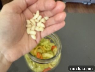 Adding peeled and sliced garlic cloves to a jar of banana pepper slices.