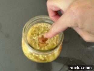 Pouring cooled pickling brine over banana pepper slices in a jar, with a weight to keep them submerged.