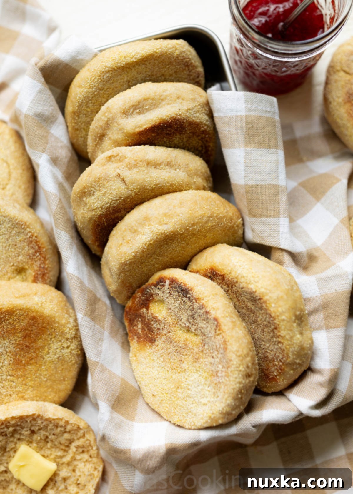 Whole Wheat English muffins arranged on a farmhouse kitchen towel in a bread pan, showcasing their golden-brown exterior and classic shape