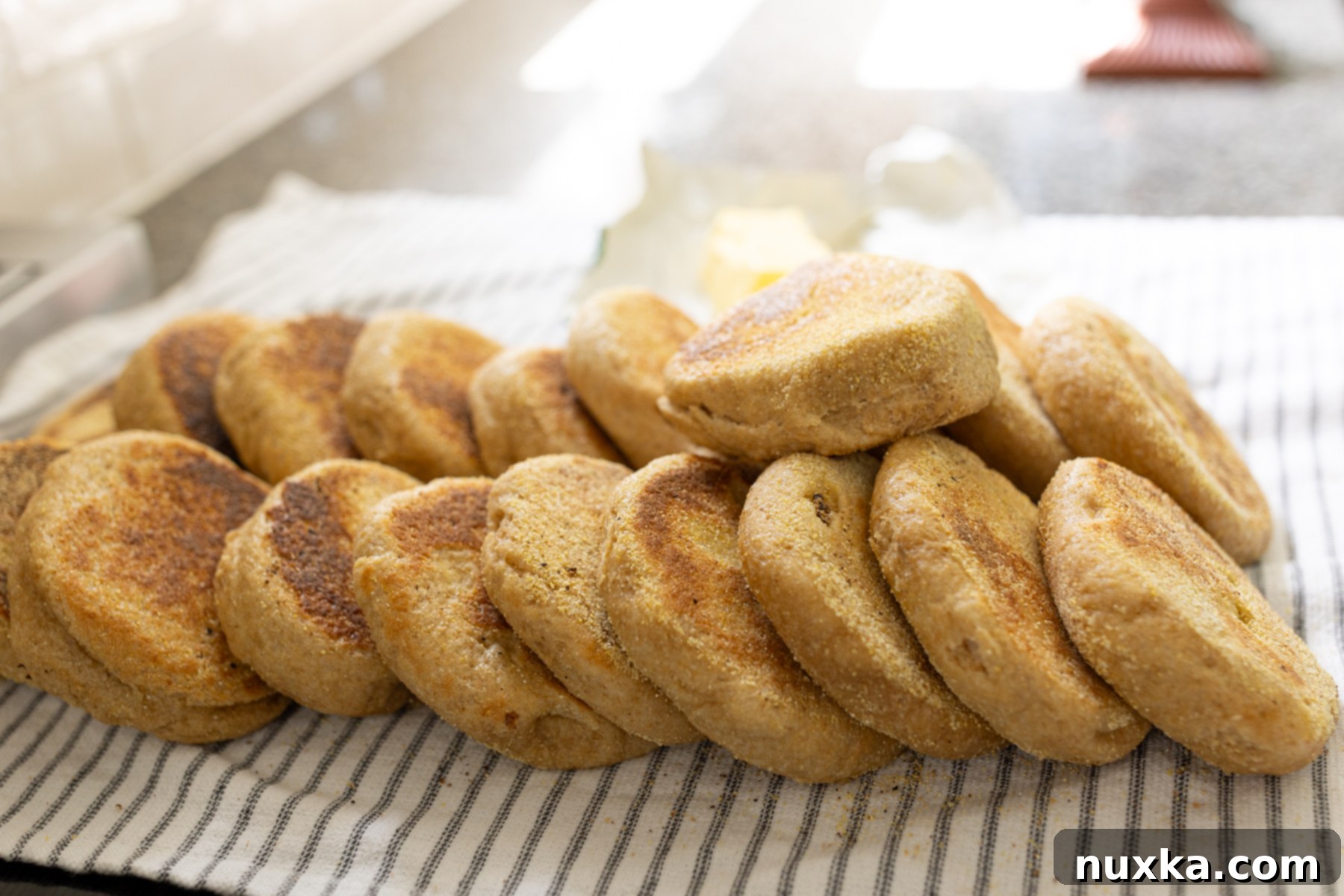 A large batch of fluffy homemade whole wheat English muffins, made from fresh milled flour, cooling on a rack in a farmhouse kitchen