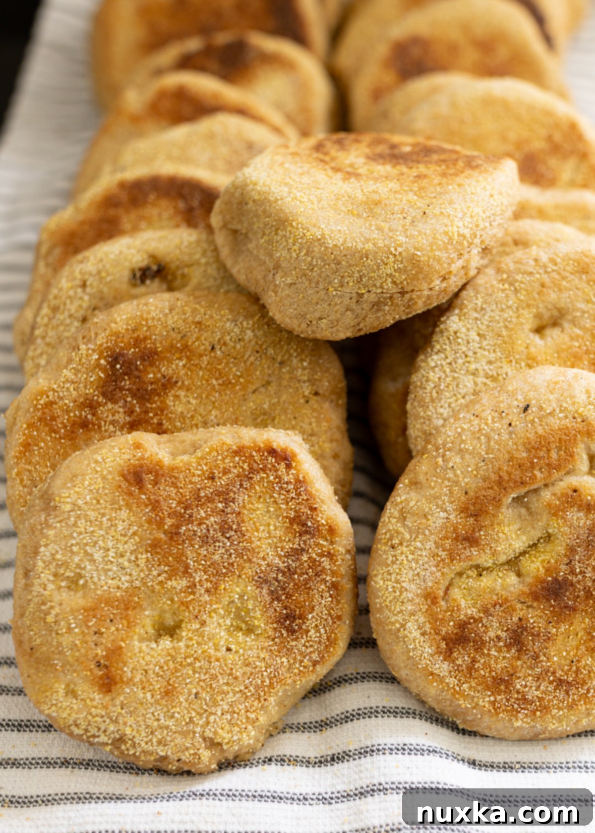 A collection of whole wheat English muffins, made from scratch, resting on a rustic kitchen towel, ready to be enjoyed