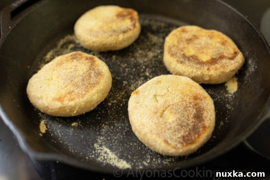 Freshly cooked Whole wheat English muffins sizzling on a cast-iron skillet, showcasing their golden-brown color and readiness