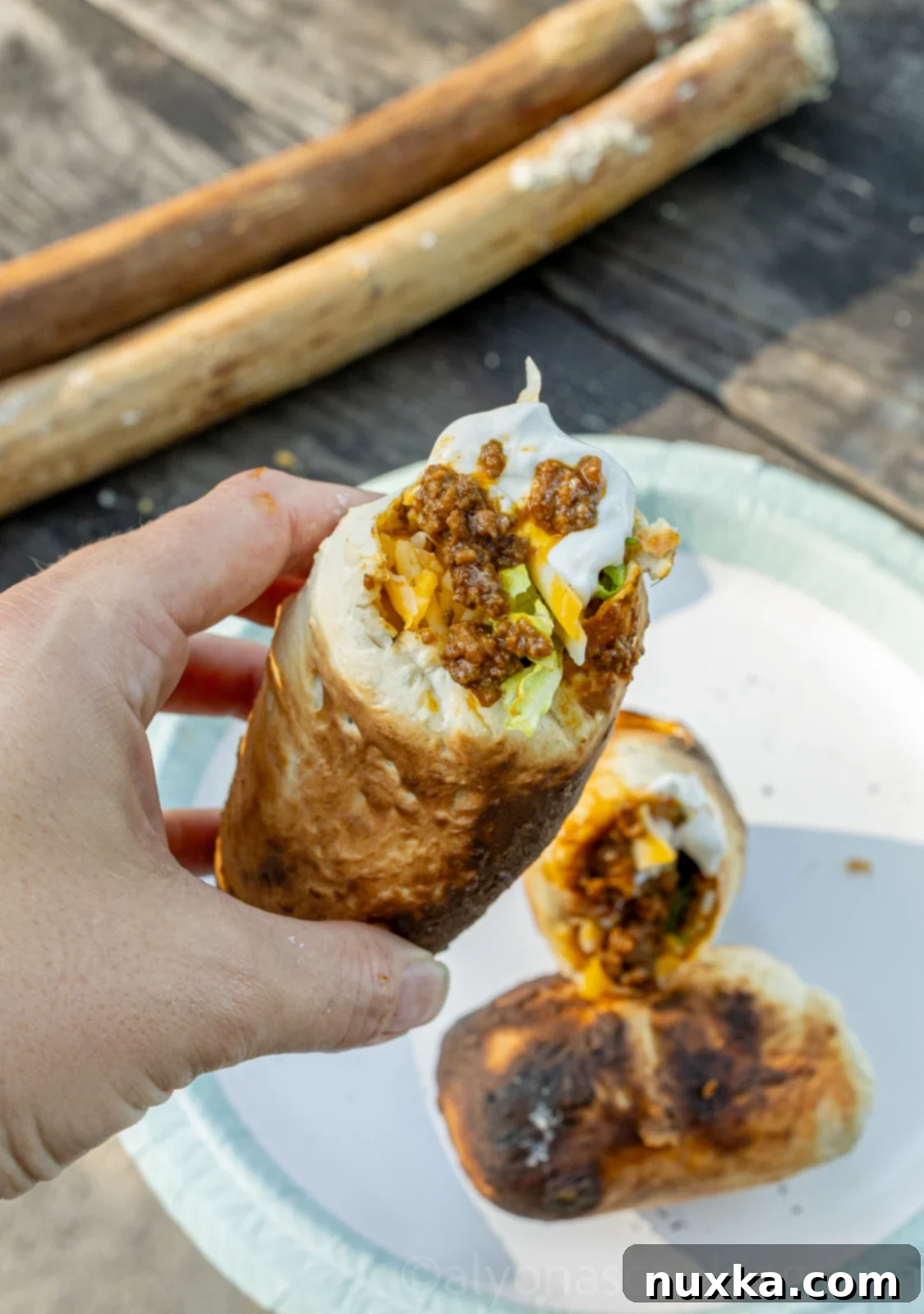 Delicious Woof Em Sticks filled with taco meat, lettuce, cheese, and salsa, held outdoors by a campfire