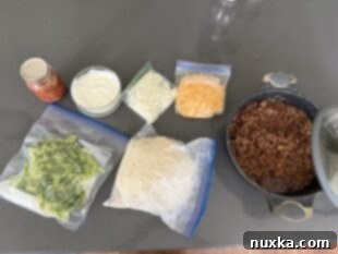 Various prepped taco ingredients including chopped vegetables, homemade biscuit dough, taco meat, shredded cheese, sour cream, and pico de gallo, ready for camping