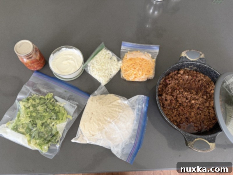 Assortment of prepped taco ingredients including seasoned ground beef, chopped lettuce, diced onions, shredded cheese, salsa, and homemade biscuit dough for Woof Em Sticks