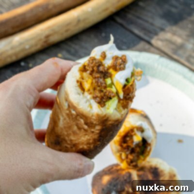 Close-up of a Woof Em Stick filled with seasoned taco meat, shredded cheese, and fresh toppings, ready to eat outdoors