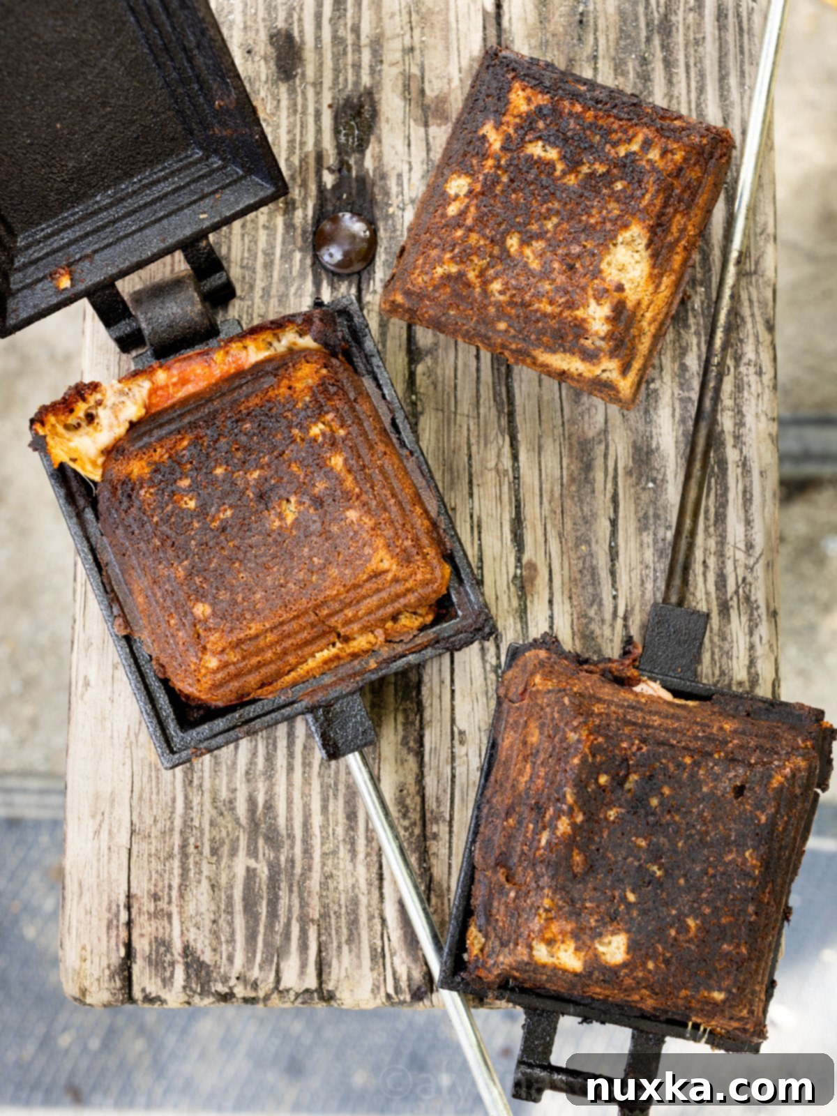 Image of Mountain pies in a mountain pie maker on a picnic table (pizza sandwich, ham and cheese sandwich, and breakfast ham, egg, and cheese sandwich)